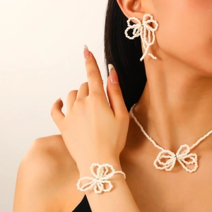 Elegant white beaded jewelry set with bow-shaped necklace, bracelet and earrings on model