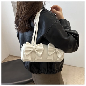 Close-up of white cylindrical shoulder bag featuring oversized decorative bows and thin straps