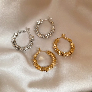 Macro shot of gold and silver irregular hammered texture hoop earrings on satin
