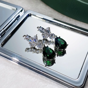 Macro detail of silver floral earrings featuring pear-cut green emerald stones and zircons