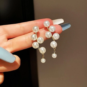 Detail of C-shaped drop earrings with white pearls and gold base on ear
