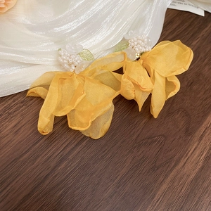 Detailed shot of yellow chiffon flower earrings with white beaded centers on wood
