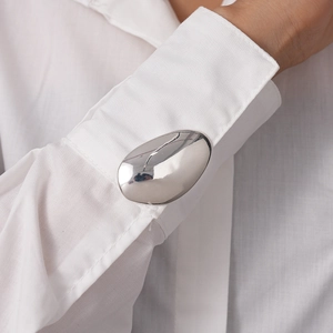 Close-up of a large oval silver cufflinks on a white shirt sleeve with mirror finish