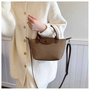 Detail of woven mini tote bag with leather flap and strap held by model in knit cardigan