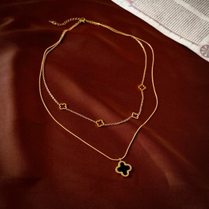 Détail d'un collier doré double épaisseur avec trèfles noirs sur satin rouge profond