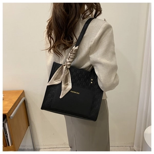Detail of black tote bag with woven texture, golden lettering and silk scarf decoration