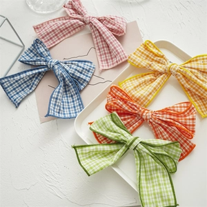 Set of five colorful checkered fabric bow hair clips displayed on a white tray and pink card