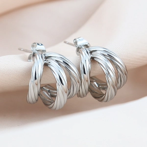 Three-layer twisted silver earrings on beige silk fabric from a high-angle view