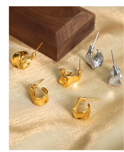 Macro view of gold and silver irregular C-shape geometric earrings on satin background