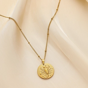 Detailed view of Scorpio zodiac gold pendant necklace on silky fabric background