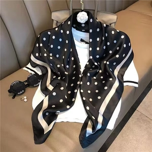 Detail shot of a black silk-feel square scarf with classic white polka dots and border