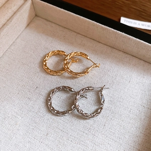Macro shot of twisted metal hoop earrings in gold and silver on a beige linen tray
