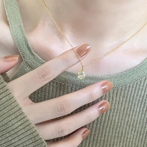 Close-up of a delicate gold chain necklace with a single round zircon pendant on a model