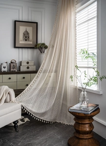 Close-up of beige crochet lace curtain with hollow floral patterns and fringe details