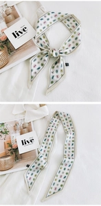 Detail of silk-like narrow scarf with leaf pattern and elegant bow tied on white fabric