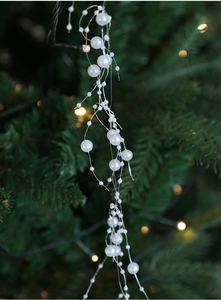 Detail of white pearl garland hanging on a Christmas tree with warm blurred bokeh lights