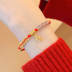 Gros plan d'un bracelet tressé rouge avec pendentif serpent doré et perles au poignet