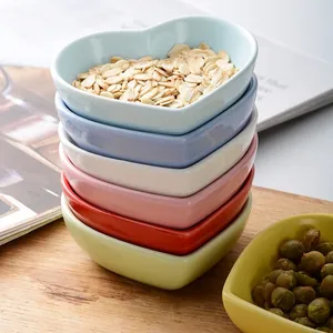 Colorful heart-shaped ceramic dipping bowls set stacked on a rustic wooden table
