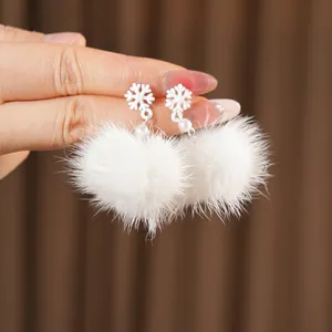 Hand holding snowflake earrings with white fur balls and pearls in a warm winter style