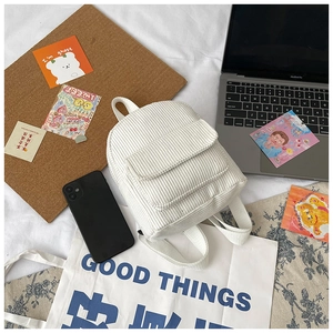 Mini white corduroy backpack detail with ribbed texture and front pocket in desk scene