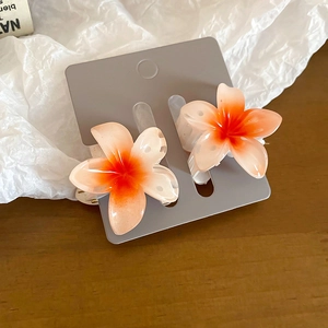 Detail of two resin frangipani hair claws with orange and pink gradient petals
