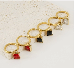 Detailed view of gold earrings with square-cut zircon charms in red, black, and clear colors