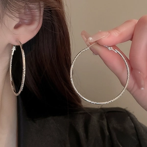 Macro detail of silver geometric hoop earrings with textured finish and zircon setting