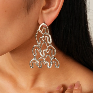 Close-up of silver geometric distorted earrings with crystals worn by a model