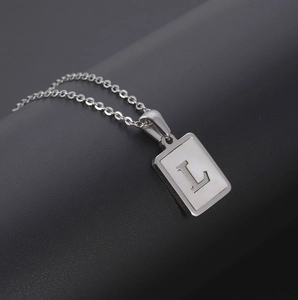 Macro shot of a silver rectangular pendant featuring a white shell inlay and hollow letter L