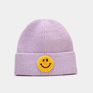 Gros plan du bonnet en tricot violet avec un écusson smiley jaune brodé sur le devant