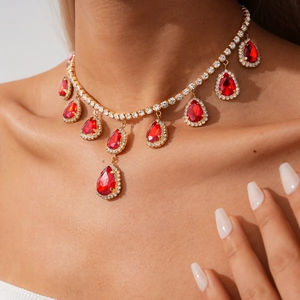 Gros plan d'un collier doré luxueux avec pendentifs goutte en cristal rouge sur modèle