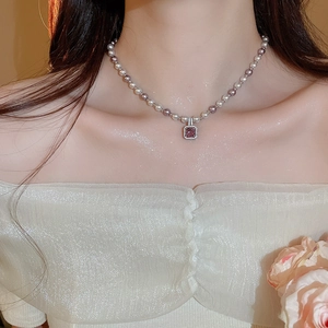 Detail of beaded pearl necklace featuring a purple zircon pendant on a female model