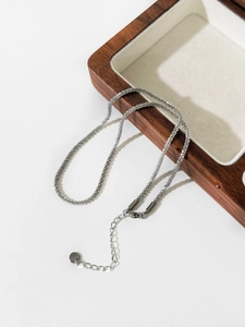 Detail of adjustable silver chain and minimalist round metal tag on a jewelry display