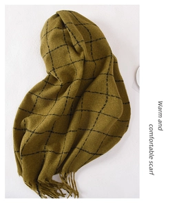 Close-up of olive green plaid scarf with soft tassels on a white textured backdrop