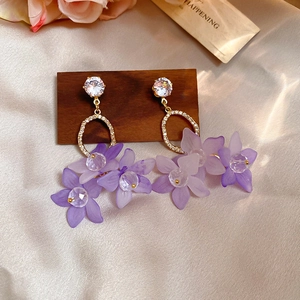Detailed macro view of violet floral pendant earrings with zircons on silk fabric