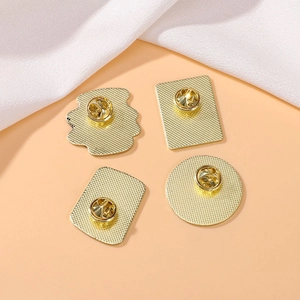 Set of four gold metal enamel pin backings with butterfly clasps on a warm background
