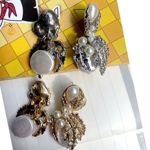 Close-up of baroque pearls and ornate metal leaf earrings in gold and silver finish