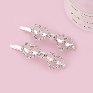 Silver hair clips with heart-shaped crystals on a soft pink background