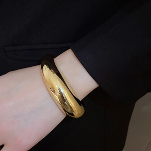 Gros plan d'un large bracelet doré poli avec effet miroir au poignet et blazer noir élégant