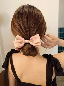 Detail of pink satin layered bow hair clip with engraved gold metal charm on back