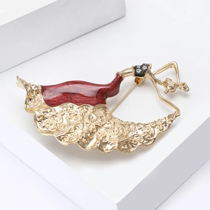 Detail of red enamel and gold-plated peacock dancer brooch on white pedestal