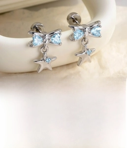 Macro shot of silver bow earring with blue heart zircon and dangling star charm detail