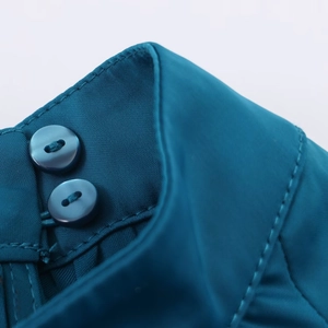 Vue macro d'une robe midi en satin bleu-vert avec double bouton et finitions soignées