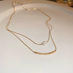 Detailed close-up of double-layer gold necklace featuring a pearl and textured curved tube