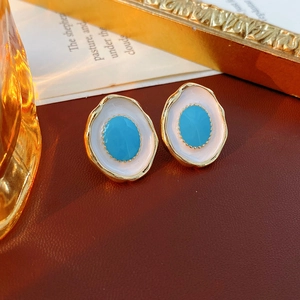 Detailed close-up of vintage oval enamel earrings with blue center on leather surface