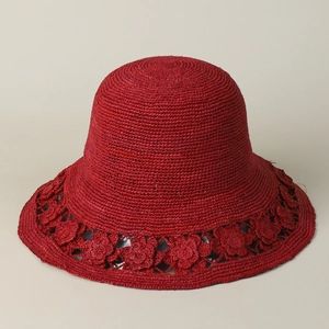 Detail of red handmade raffia sun hat with hollow floral crochet patterns on the wide brim