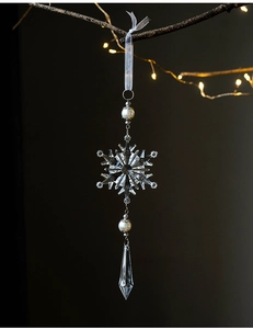 Detail of a clear acrylic snowflake ornament with faux pearls on a festive branch