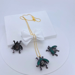 Detail of gold necklace and beetle earrings set with green cubic zirconia on white stand