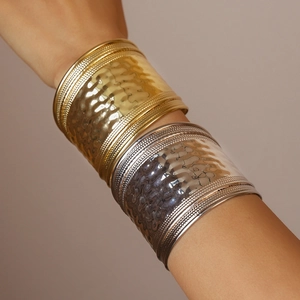 Detail of wide hammered metal cuff bangles in gold and silver finish with beaded edges