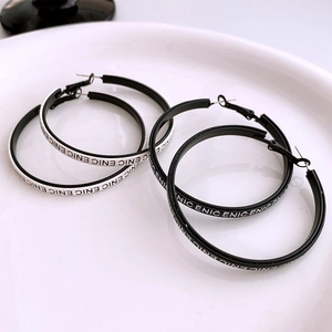 Detail of large black and silver monochrome hoop earrings with repeating ENIC text pattern